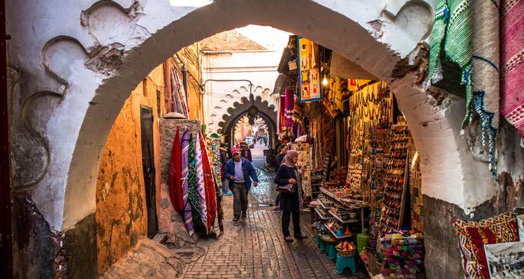 A narrow alleyway in a market with colorful textiles and goods.