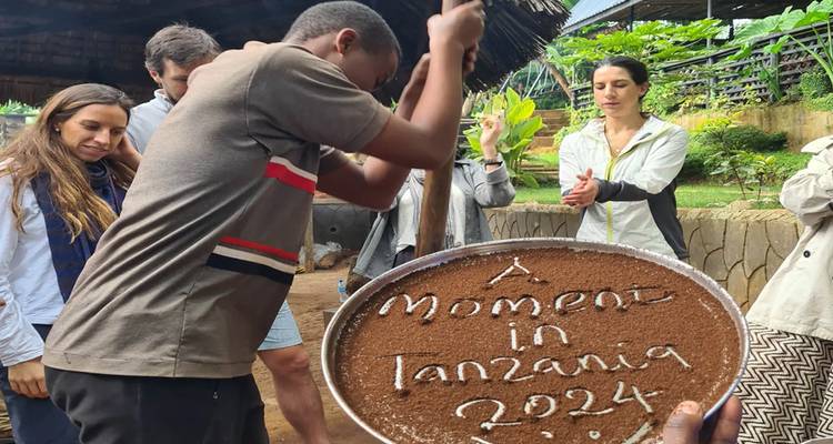Gruppe genießt Kaffeezubereitung in Tansania mit einem Schild mit der Aufschrift 'Ein Moment in Tansania 2024'.