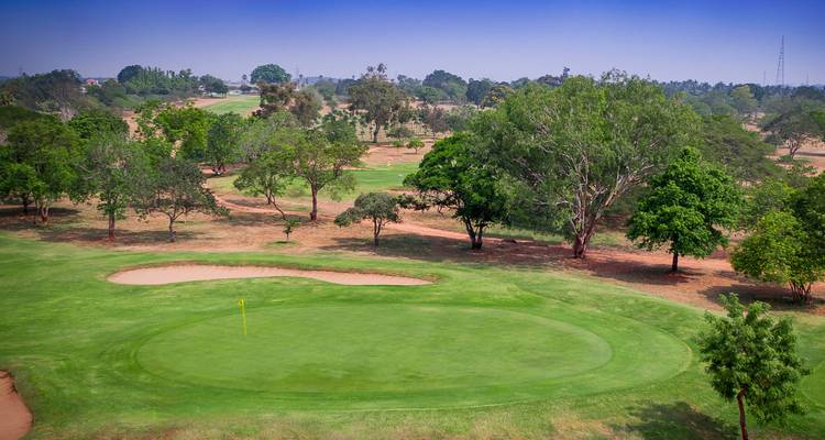 Una vista panorámica de un campo de golf con césped verde y árboles circundantes bajo un cielo azul despejado.