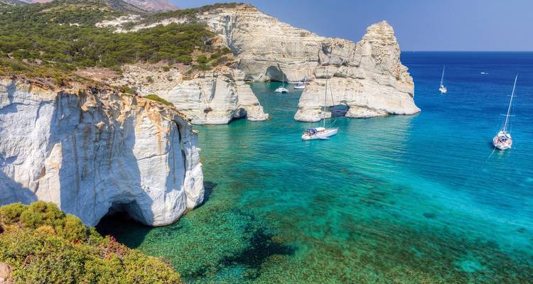 Coastal rock formations with boats on turquoise water.