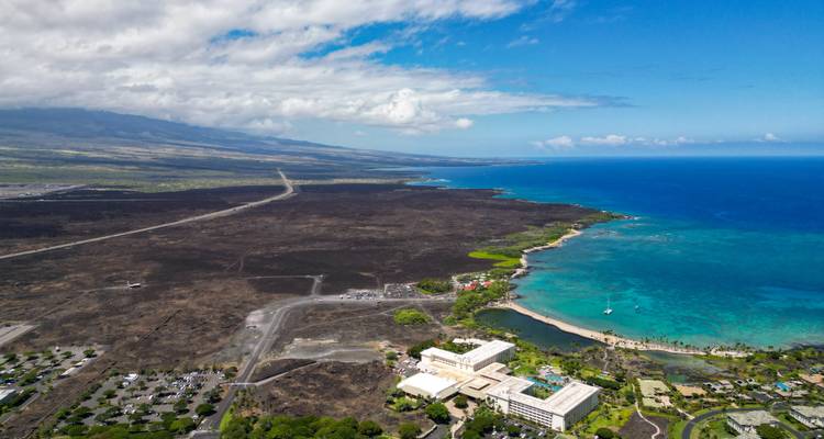 Aerial view of a coastal resort with blue ocean and dark volcanic fields