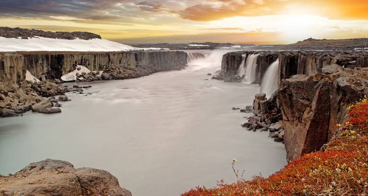 Cañón amplio con múltiples cascadas cayendo en un río brumoso al amanecer.