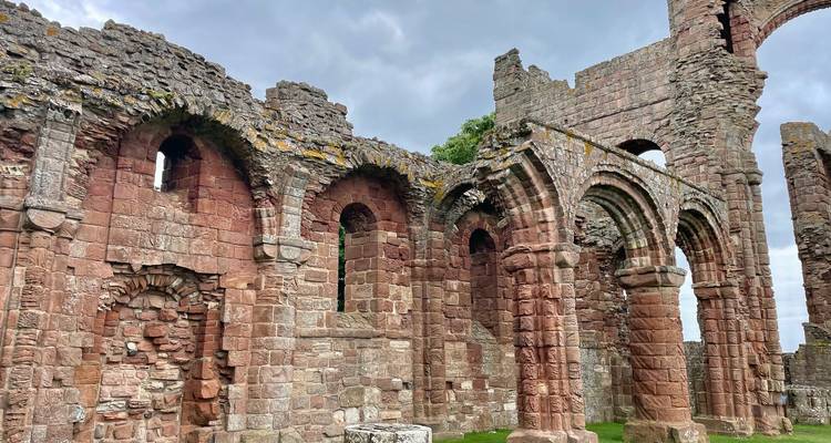Ruines en grès rouge usé d'une abbaye médiévale se détachant sur un ciel gris morose.