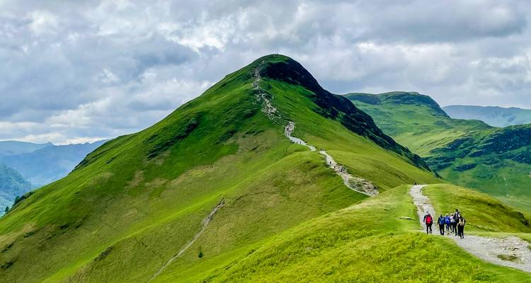Les randonneurs traversent la crête verdoyante de Cat Bells avec des pics spectaculaires et un sentier sinueux qui s'étend devant eux.