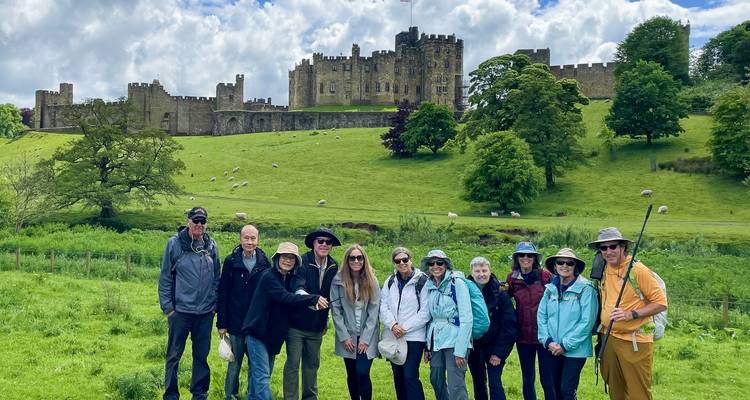 Un groupe de randonneurs posent devant le château d'Alnwick sur une colline verdoyante luxuriante.