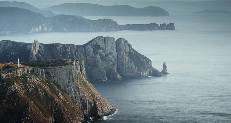 Cliffs and ocean with a lighthouse in the distance.