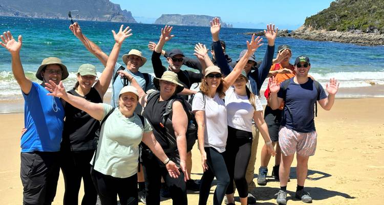 Group of people on a beach waving at the camera.