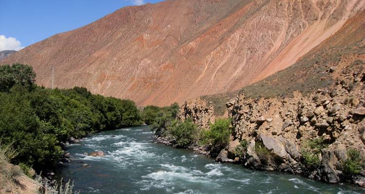 Rivière traversant une vallée rocheuse avec des arbres verts et des collines.