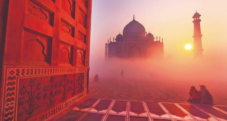 Taj Mahal en la niebla con puesta de sol y gente en primer plano.