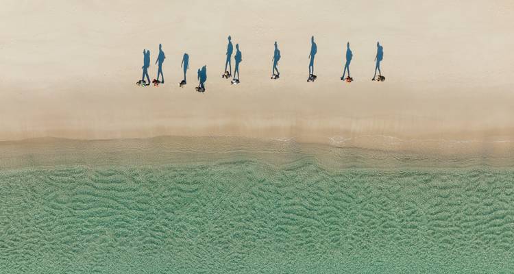 Luchtfoto van een strand met schaduwen van mensen op het zand.