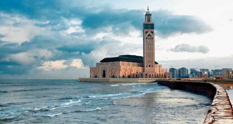 Mosque by the ocean with city skyline in the distance.