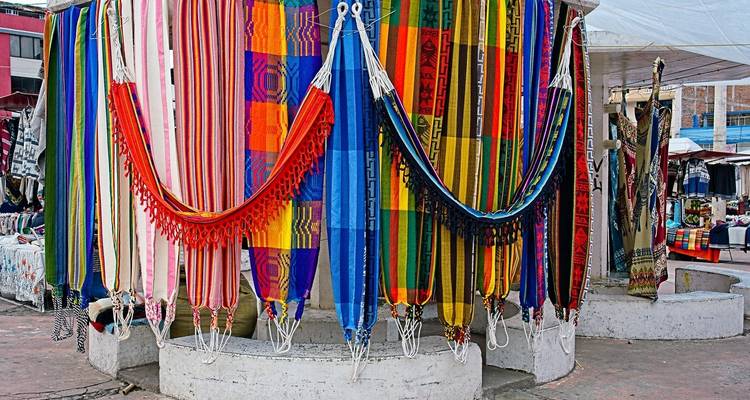 Kleurrijke geweven textielen die in een markt hangen.