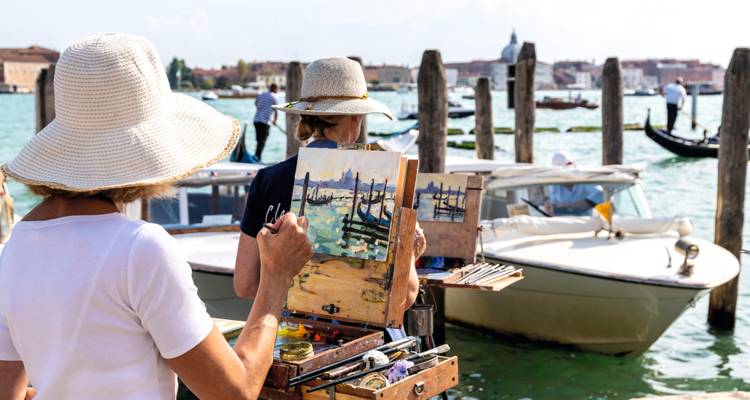 Artists painting a canal scene en plein air beside bobbing boats and gondolas on the Venetian lagoon.