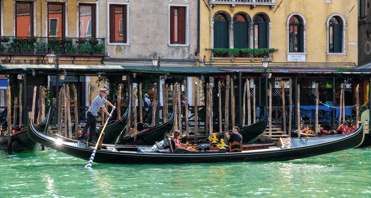 Classic gondola with a gondolier rowing passengers past vibrant historic buildings on Venice’s Grand Canal.