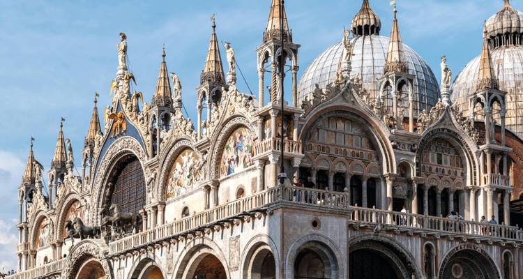 Ornate façade and domes of St Mark’s Basilica against a blue sky.
