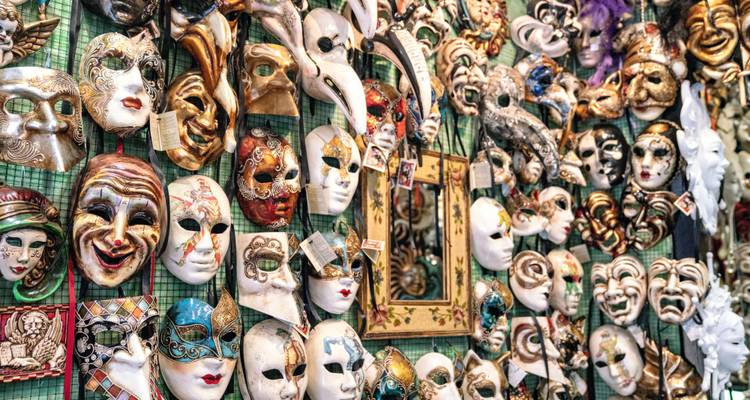 Colorful display of traditional Venetian carnival masks hanging on a shop wall.