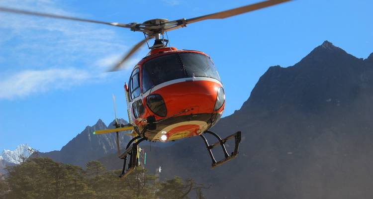 Hélicoptère orange volant devant un paysage montagneux.