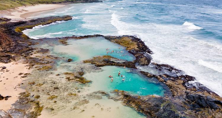 Aerial view of natural pools by the ocean with people swimming.