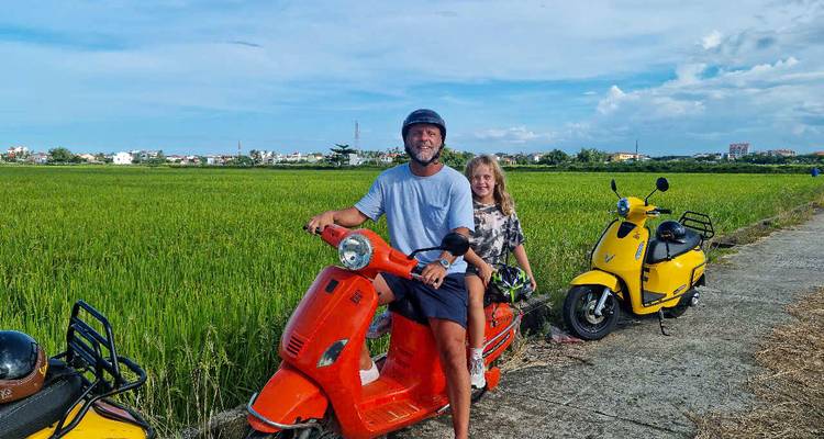 Personne et enfant sur un scooter rouge et un scooter jaune dans un champ.