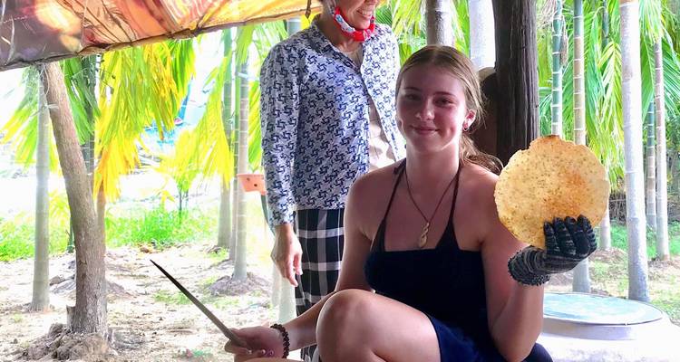 Deux personnes sous un auvent tenant un biscuit de riz, entourées de palmiers.