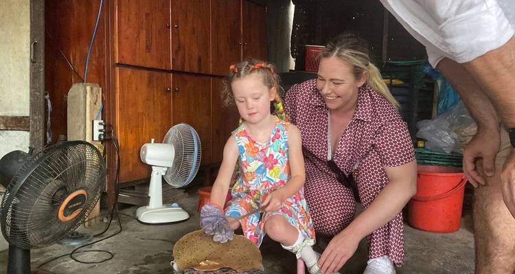 Niña pequeña asistida por su madre voltea una galleta de arroz en una cocina casera sencilla.