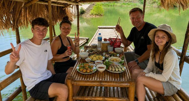 Famille savourant un repas vietnamien sur un radeau en bambou flottant au-dessus d'un lac vert tranquille.