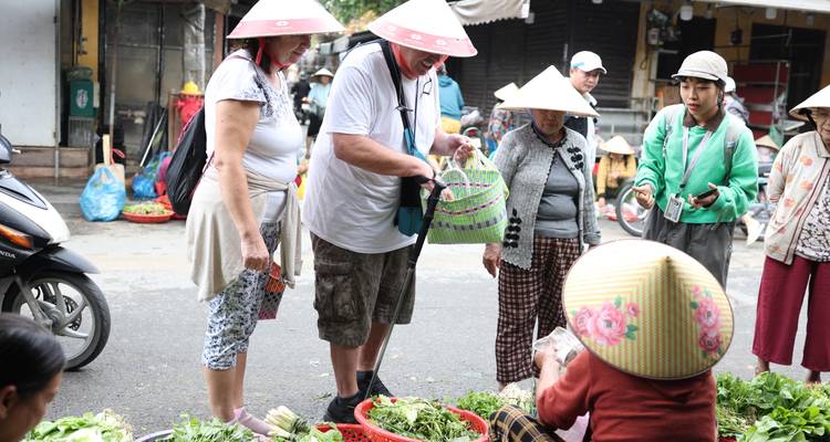 Les visiteurs portant des chapeaux coniques négocient l'achat de légumes frais sur un marché de rue vietnamien animé.