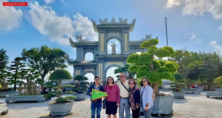 Tourists posing in front of a large decorative archway with a clear sky backdrop.