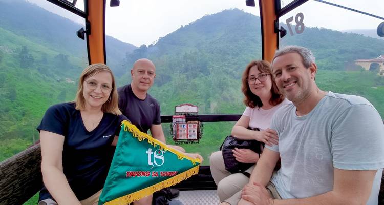 Four people in a cable car with lush green mountains visible outside.