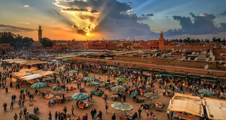 Busy market square at sunset with numerous stalls and people.