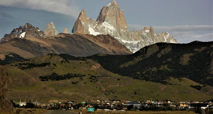 Paysage montagneux avec une petite ville à la base, des sommets enneigés en arrière-plan.