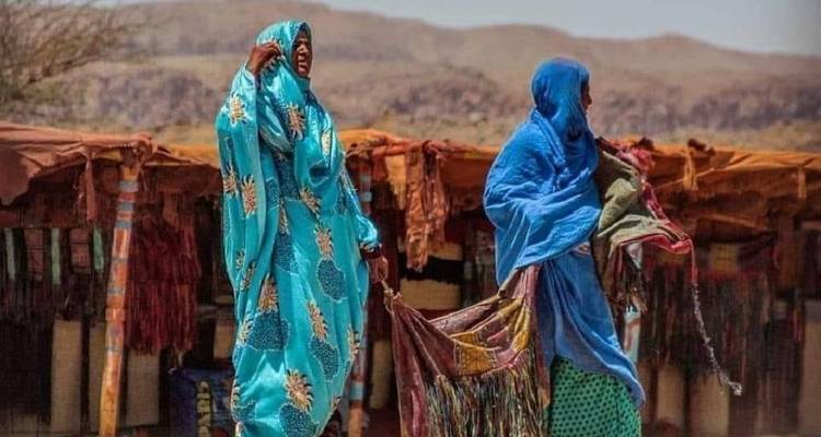 Two people in traditional clothing holding textiles in a marketplace.