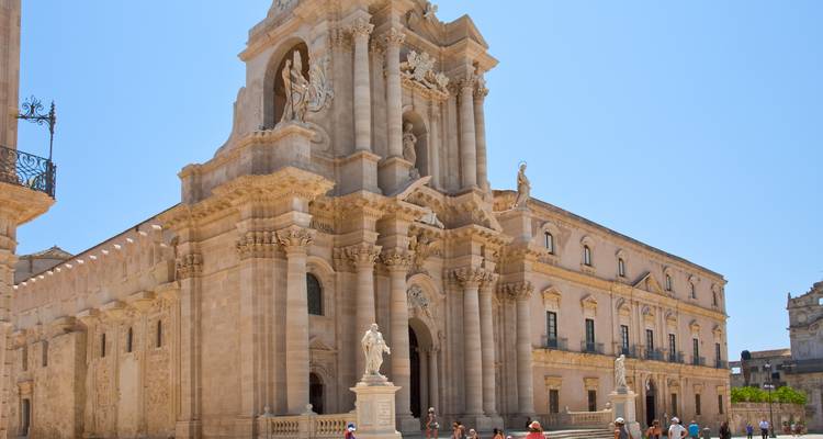 Gran catedral con fachada ornamentada y estatuas, personas caminando en frente.