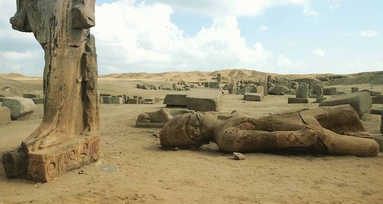 Oude beelden en vervallen ruïnes in een zanderig gebied.