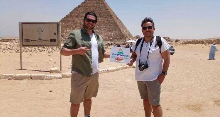 Twee mannen poseren bij een piramide met een heldere hemel.