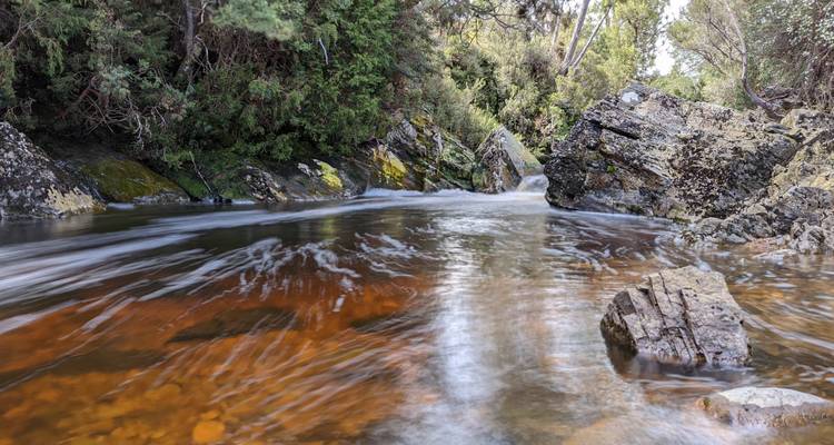 Rivière tranquille coulant entre des rives rocheuses et des forêts.
