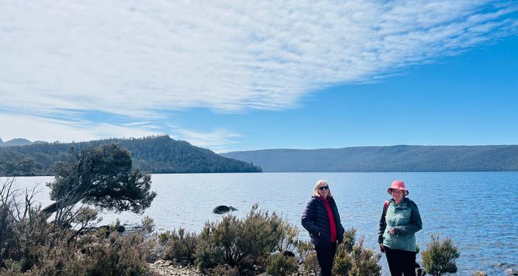 Deux femmes debout près d'un lac avec des collines en arrière-plan.