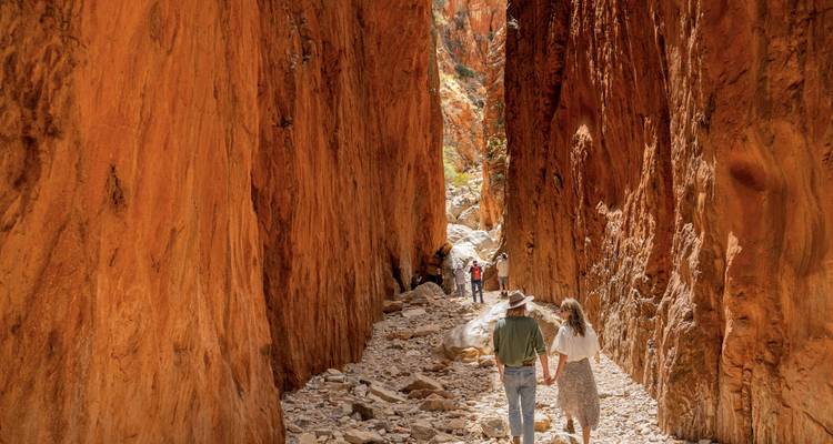 Couple marchant à travers une gorge étroite avec de hautes parois rocheuses orange.