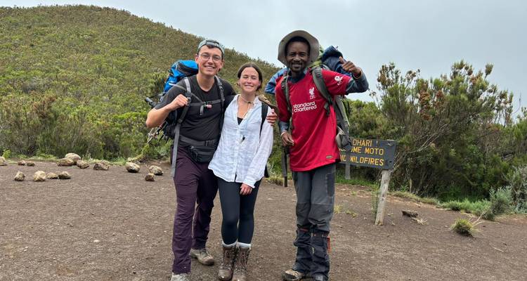 Trois randonneurs posant dans un paysage montagneux avec un panneau.