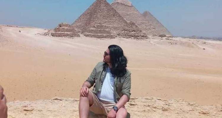 Person, die in der Wüste sitzt mit Pyramiden in der Ferne.