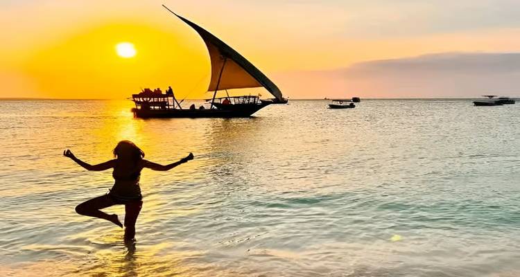 Person im Wasser posiert vor einem Sonnenuntergang mit einem Segelboot.