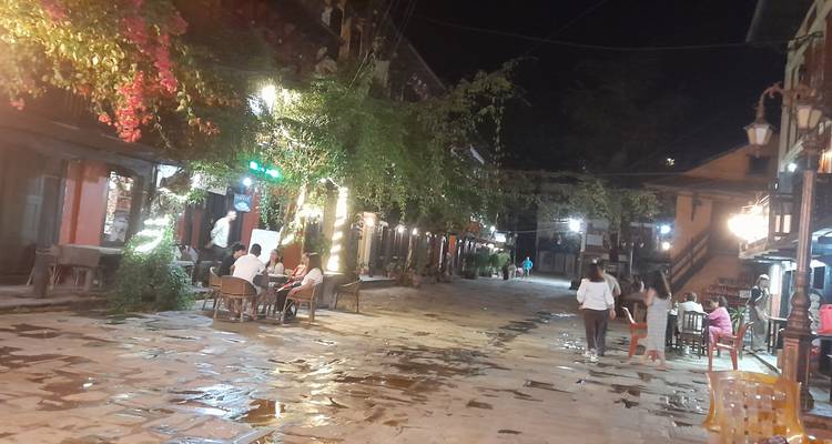 Une vue de rue mouillée et illuminée avec des gens assis à des tables la nuit.