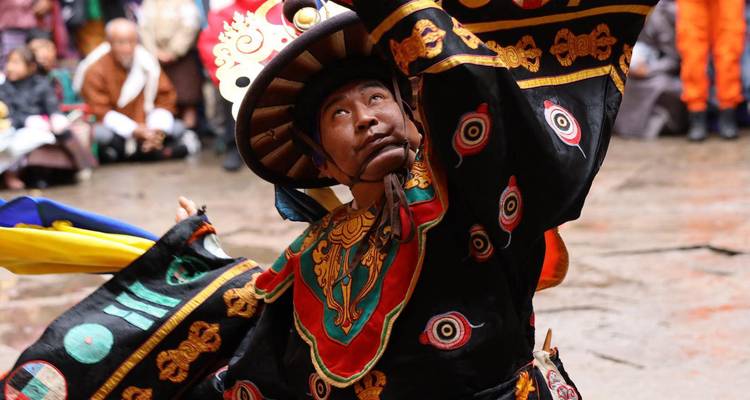 Primer plano vibrante de un bailarín enmascarado en un traje negro ornamentado actuando en un festival bhutanés.