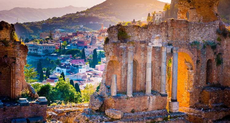 Ruines antiques avec colonnes sous un arrière-plan montagneux avec une ville.