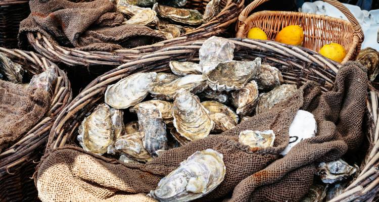 Close-up van verse oesters hoog opgestapeld in rustieke rieten manden op een buitenmarkt.
