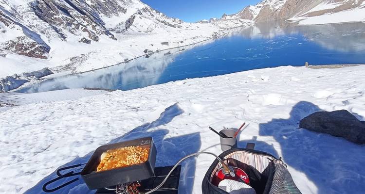 Een besneeuwde berglandschap met een bevroren meer, kookgerei zichtbaar op de voorgrond.
