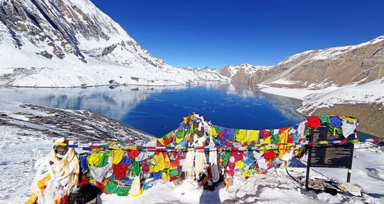 Kleurrijke gebedsvlaggen naast een bevroren meer en besneeuwde bergen.