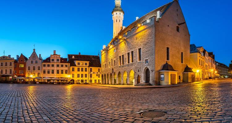 La Plaza del Ayuntamiento empedrada de Tallin brillando con la luz azul del crepúsculo y las cálidas luces de los edificios.