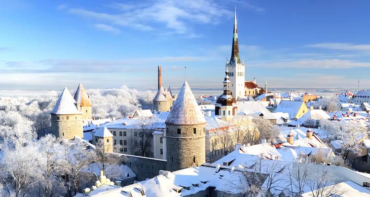 Las torres medievales y el campanario de la iglesia de Tallin cubiertos de nieve blanca fresca bajo un cielo azul despejado.