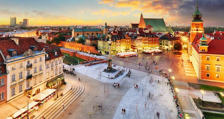 Puesta de sol vibrante sobre la Plaza del Castillo de Varsovia con multitudes animadas, edificios históricos y la Columna de Segismundo.